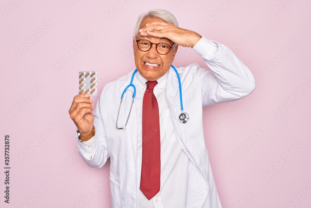 Sticker Middle age senior grey-haired doctor man holding prescription pills over pink background stressed with hand on head, shocked with shame and surprise face, angry and frustrated. Fear and upset