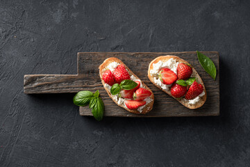Fototapeta na wymiar bruschettas with strawberries, cream cheese and basil on a wooden board on a black background