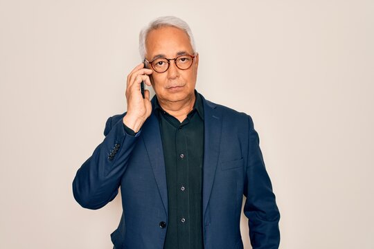 Middle age senior grey-haired business man wearing glasses talking on smartphone with a confident expression on smart face thinking serious