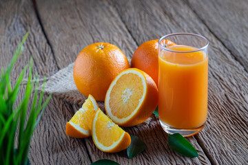 Glass squeezed orange juice and fresh fruits ripe cut half, slice with green leaves on wood table.