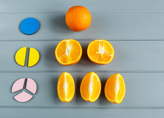 Close up mathematical fractions and oranges as a sample of parts on gray background. Creative, fun...