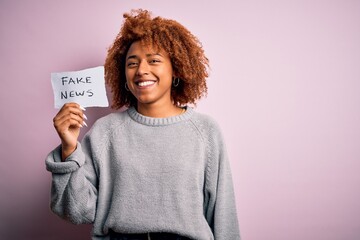 Young African American afro woman with curly hair holding paper with fake news message with a happy...