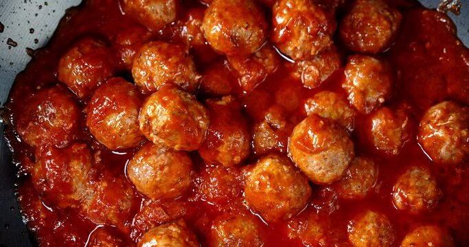 Cooking meatballs in tomato sauce in the pan with air bubbles.