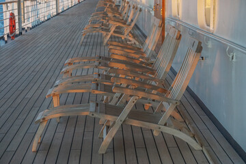 A long row of empty deck chairs on the Promenade Deck of a cruise ship, in the early evening.