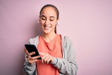 Naklejka premium Beautiful sporty woman doing sport listening to music using earphones over pink background with a happy face standing and smiling with a confident smile showing teeth