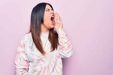 Young beautiful brunette woman wearing casual dyed sweatshirt over isolated pink background shouting and screaming loud to side with hand on mouth. Communication concept.