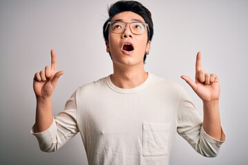 Young handsome chinese man wearing casual t-shirt and glasses over white background amazed and...