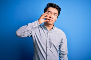 Young handsome chinese man wearing casual shirt standing over isolated blue background mouth and lips shut as zip with fingers. Secret and silent, taboo talking