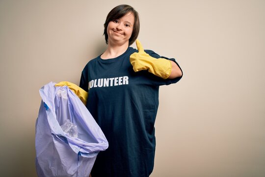 Young down syndrome volunteer woman picking rubbish and plastic from the trash happy with big smile doing ok sign, thumb up with fingers, excellent sign