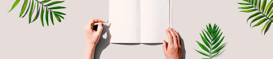 Person writing in a notebook with tropical leaves from above