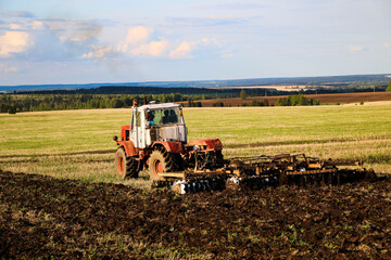  tractor plows and harrows  land in  large field on  sunny spring day. preparing  soil for planting crops, plowing  soil with  tractor with  disk plow.