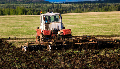 Fototapeta na wymiar tractor plows and harrows land in large field on sunny spring day. preparing soil for planting crops, plowing soil with tractor with disk plow.