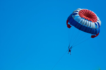 red white blue parachute attraction/parasailing flies on blue clear sky. isolated on blue for...