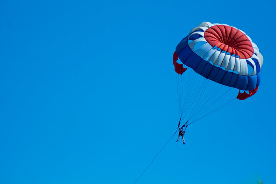 red white blue parachute attraction/parasailing flies on blue clear sky. isolated on blue for background and wallpaper