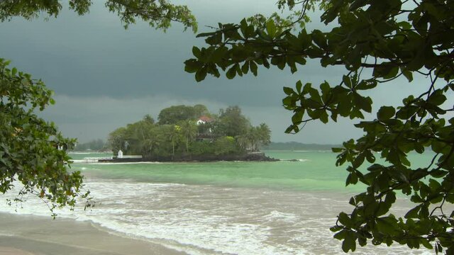 Tilt down shot of house amidst trees on island surrounded by waves in sea against cloudy sky - Arugam Bay, Sri Lanka