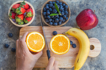 Lady cutting orange on wooden board with multi fruit frome top view.