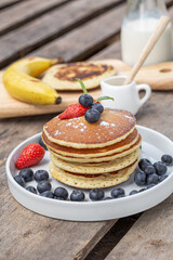 Pancake with fresh berries on white plate for breakfast with banana and milk on wooden table