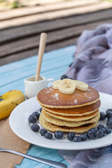 Pancake with fresh blueberries and banana on white plate for breakfast on blue wooden table