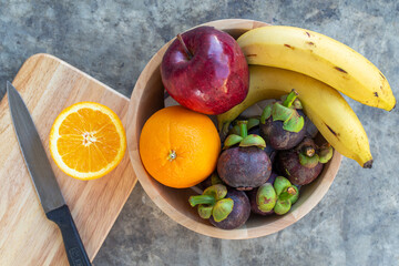 Cutting orange on wooden board with multi fruit in wooden bowl frome top view.