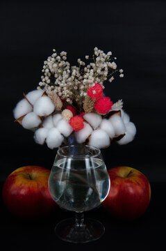 art photo glass of water two apples and a bouquet of cotton and white flowers on a black background