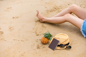 Hat, passport, pineapple  beside woman sitting on the beach. summer, holidays, vacation, travel concept