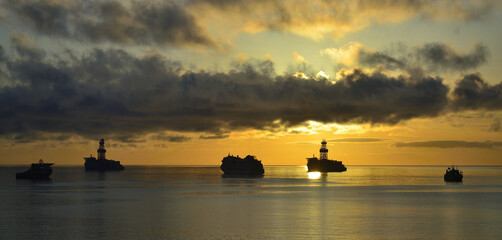 Naklejka na ściany i meble Ships anchored in the bay at sunrise, cloudy sky and calm sea
