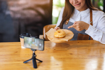 A beautiful asian woman food blogger or vlogger showing a piece of donut while recording a video on camera