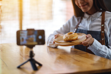 A beautiful asian woman food blogger or vlogger showing a piece of donut while recording a video on camera