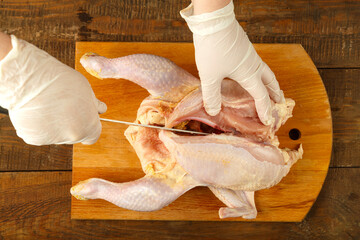 Woman cuts chicken carcass with a knife on a wooden board. © finist_4