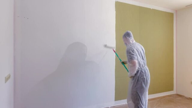 Time lapse of painter painting the wall white colour. Man in protective work clothes decorating the room with a paint roller. Home renovation. Apartment renewal concept.