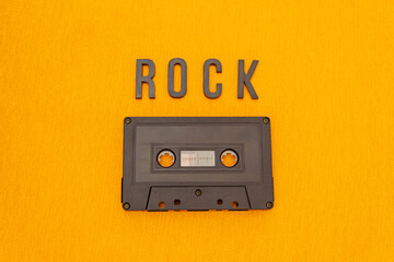 Top View of ROCK black lettering word with an old black cassette over a yellow cloth. Fashion and music concept