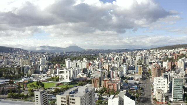 Drone shot of the North part of the city of Quito, Ecuador. Overlooking buildings and in the back, Parque La Carolina during quarantine. Also, mountains and empty streets with trees and houses.