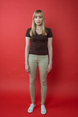 Blonde cheerful woman in brown t-shirt showing non correct (wrong) modeling, posing on red background. Beauty, fashion, youth concept