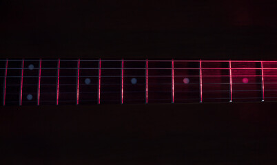 closeup to a six black electric guitar strings and wooden fretboards iluminated with red lights Instruments and music concept