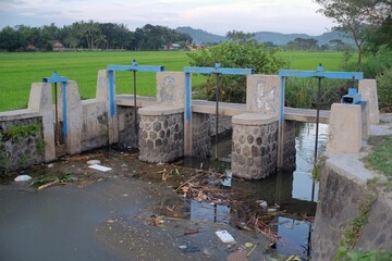 River water with a pile of garbage held in irrigation dams regulating water discharge for residents' agriculture