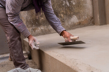 Indian labour levelling plastered floor using flat trowel and cement manually, Stock image.
