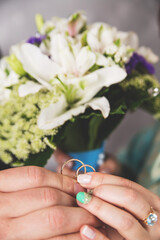 Fototapeta premium Hands of newlyweds with wedding rings and a bouquet of flowers. A bouquet of white cream roses and lilac flowers of the field. Concept of love wedding and Valentine's Day