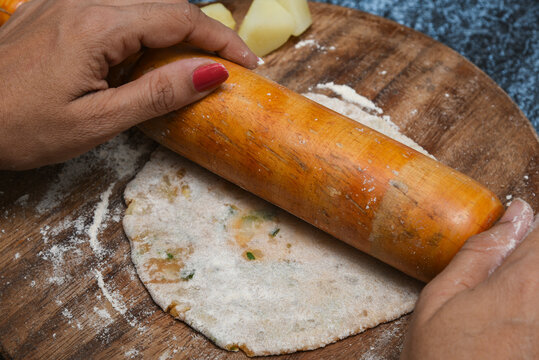 Preparation of Aloo Paratha or roti parantha chapati Punjab, North India. Female hand rolling whole wheat dough mashed potato stuffing with rolling pin. Indian side dish raita, dal makhani.