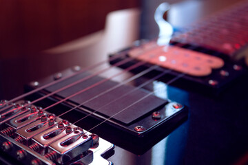 closeup to a six black electric guitar strings, wooden fretboard and microphones iluminated with...