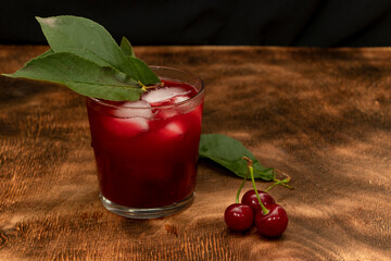 Red cocktail. Cherry juice with ice. Cherry leaves and cherry berries. The summer aroma of coolness in a glass. Juccy.