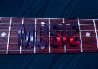 Closeup to a ROCK lettering black word over a six electric guitar strings and wooden fretboard iluminated with white and red colors. Rock & Roll, instrument and music concept