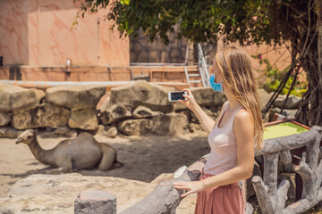 Fototapeta premium Young woman at the zoo in a medical mask. Visiting public places after the coronavirus epidemic
