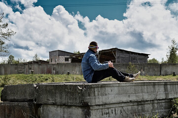 Photo of the ruins of a building. A man in a protective mask sits on the ruins in sunny weather.