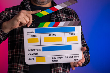 Homem com camisa xadrez escura segurando Claquete de Cinema com fundo azul e rosa neon - Imagem...