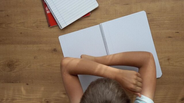 Kid sitting at table with open notebooks and lowered his had on the hands. Education, learning difficulties, school homework, learning at home