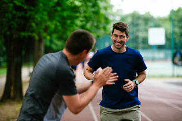  Young men training on a race track. Two young friends running on athletics track