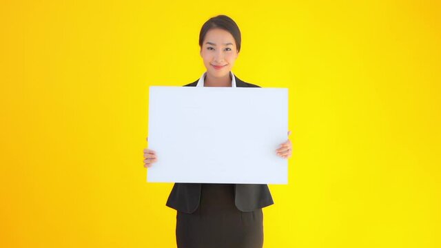 Asian businesswoman holding a blank sheet of the paper poster banner with a happy face expression on yellow studio background
