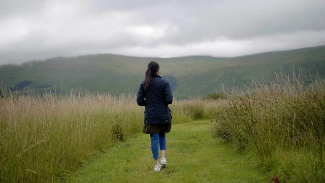 Following young woman walking trail through tall grass in Highlands of Scotland