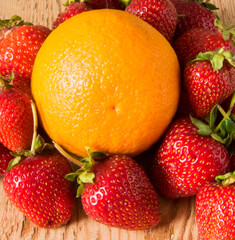 Red juicy strawberries with orange on a wooden table close-up