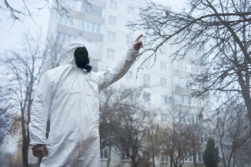 Scientist pointing up with finger, standing between autumn trees. Man in gas mask and protective...